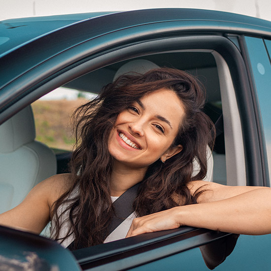 A young person smiling while sitting behind the wheel of a car